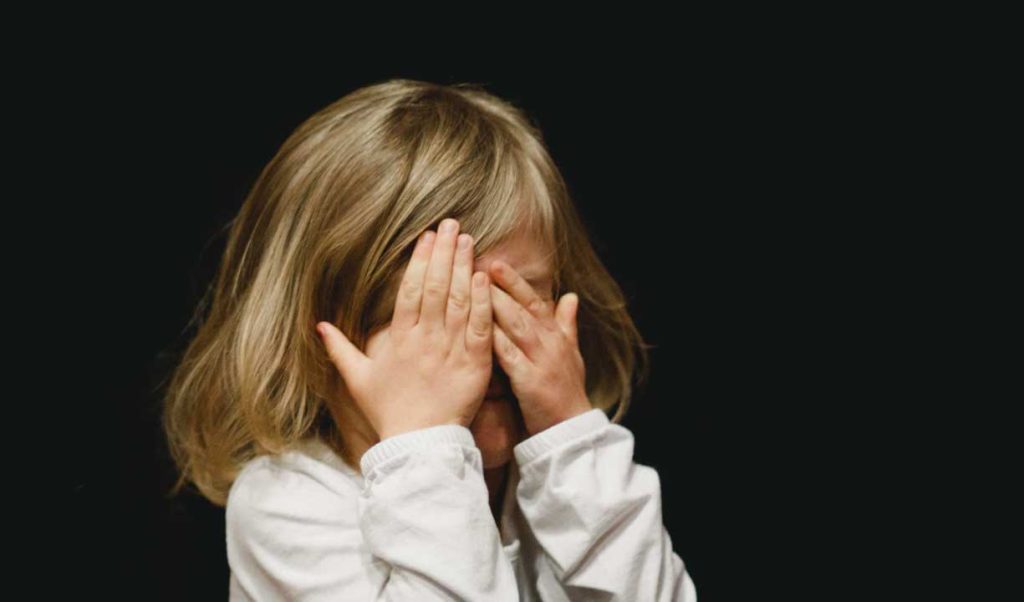 Worried or anxious child: little girl hiding her eyes with her hands